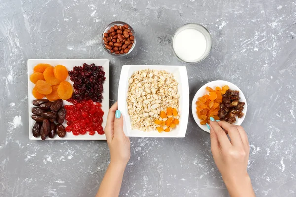 Kız onu müsli kahvaltı için hazırlanıyor. Kız kendini yulaf lapası kurutulmuş meyve koyar. Gri bir arka planda en iyi görünüm yararlı ve sağlıklı bir kahvaltı.