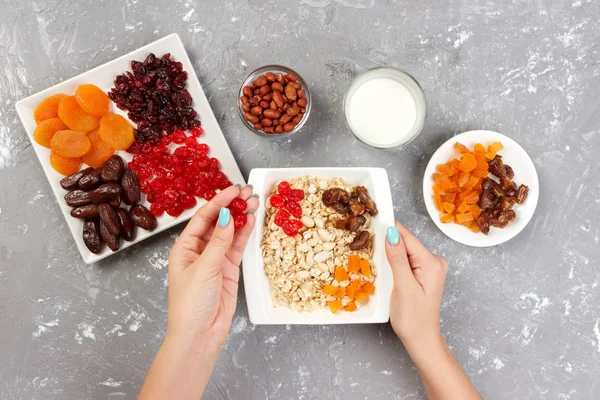 Kız onu müsli kahvaltı için hazırlanıyor. Kız kendini yulaf lapası kurutulmuş meyve koyar. Gri bir arka planda en iyi görünüm yararlı ve sağlıklı bir kahvaltı.