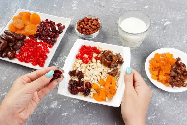 Yararlı ve sağlıklı bir kahvaltı. Kız onu müsli kahvaltı için hazırlanıyor. Kız kendini Kuru meyve yulaf lapası üstten görünüm, gri bir arka plan koyar.