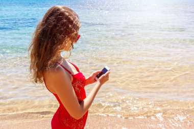 Bir akıllı telefon kullanarak mayo giyen sunbather kız. yaz tatili sahilde.