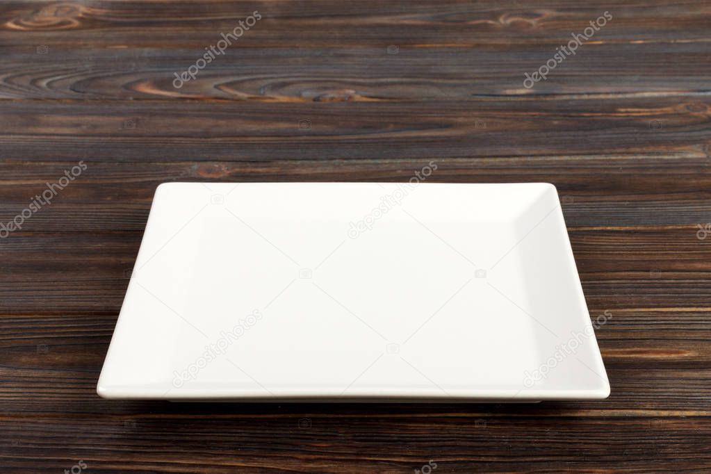 Empty square white plate in wood background, food display montage. Perspective view .