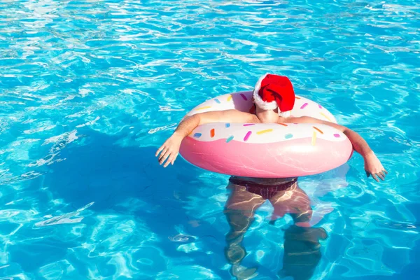 top view of young drunk guy in christmas hat swim with pink circle in pool. drunk guy on vacation in the hotel.