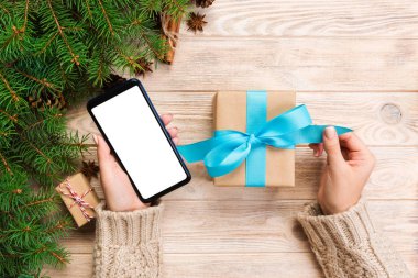 Noel hediye kutusu kaydırma ve telefon masajla mavi şerit kahverengi ahşap masa üzerinde okuma eller basılı tutun. Üstten görünüm.