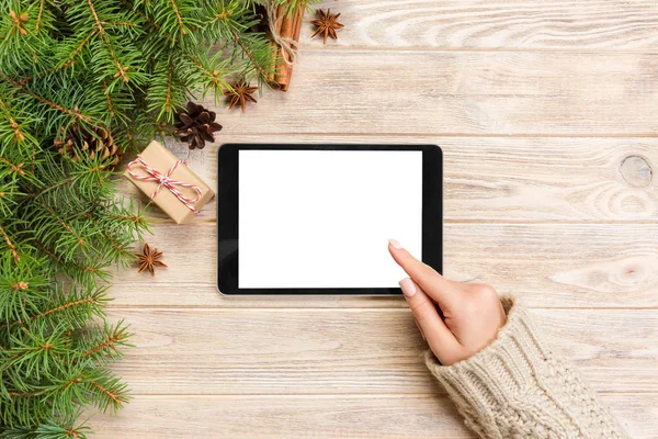 Christmas online shopping. Female hand touch screen of tablet, top view on wooden bakground, copy space. Winter holidays sales background.