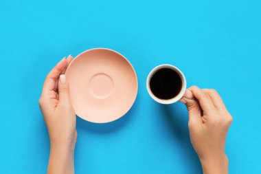 High angle of woman hands holding coffee cup on blue background Minimalistic style. Flat lay, top view isolated. clipart