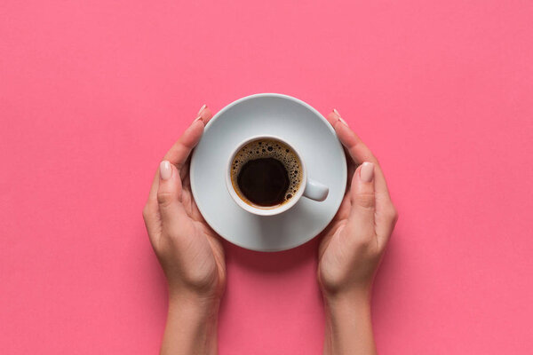 High angle of woman hands holding coffee cup on pink background Minimalistic style. Flat lay, top view isolated.