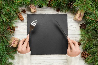 üstten görünüm kız tutar çatal ve elinde bıçak ve yemek hazırdır. Boş siyah arduvaz kare plaka ahşap Noel arka plan üzerinde. tatil yemek yemek kavramı ile Yılbaşı dekor.