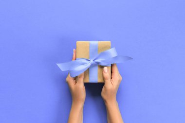 Hediye kutusu ile mor şerit renk arka plan, üstten görünüm üzerinde tutan kadın kolları.