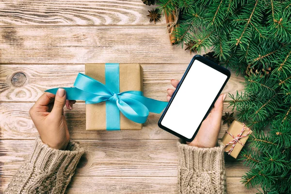 Noel hediye kutusu kaydırma ve telefon masajla mavi şerit kahverengi ahşap antika masa üzerinde okuma eller basılı tutun. Üstten görünüm.