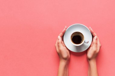 Minimalist stil bir kadın pembe arka planda bir fincan kahve tutuyor. Düz yatış, üst görünüm.