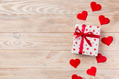 Sevgililer veya diğer tatil el yapımı mevcut kağıt ile tatil sarmalayıcı kırmızı kalpler ve hediye kutusunda. Tasarım için turuncu ahşap masa üstten görünüm kopya alanı ile boş alanı hediye kutusu.