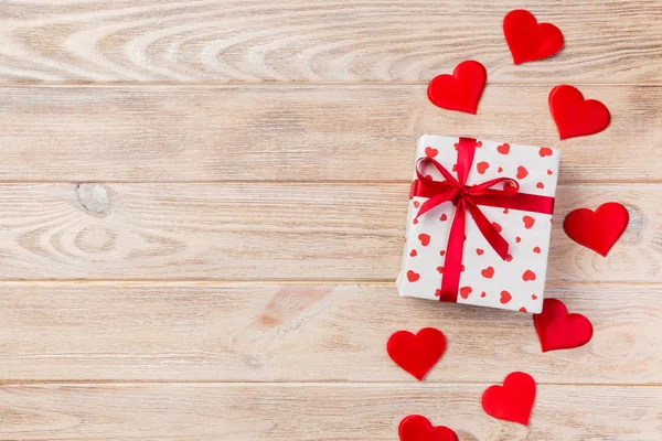 Sevgililer veya diğer tatil el yapımı mevcut kağıt ile tatil sarmalayıcı kırmızı kalpler ve hediye kutusunda. Tasarım için turuncu ahşap masa üstten görünüm kopya alanı ile boş alanı hediye kutusu.