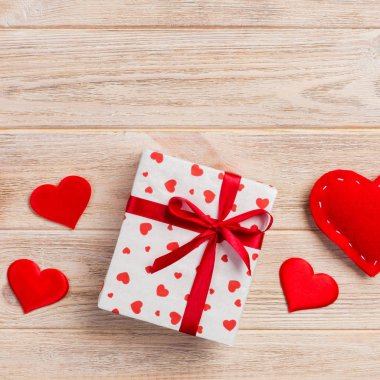 Sevgililer veya diğer tatil el yapımı mevcut kağıt ile tatil sarmalayıcı kırmızı kalpler ve hediye kutusunda. Tasarım için turuncu ahşap masa üstten görünüm kopya alanı ile boş alanı hediye kutusu.