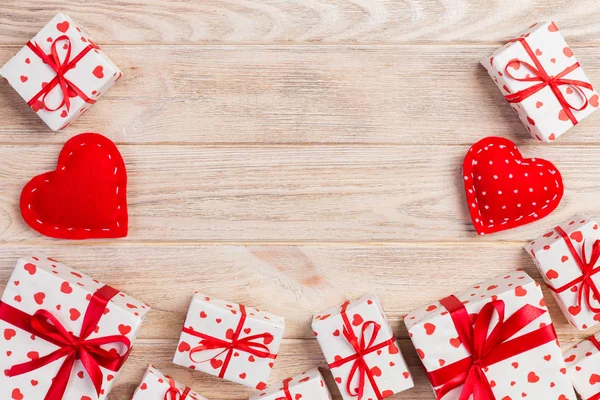 Valentine or other holiday handmade present in paper with red hearts and gifts box in holiday wrapper. Present box of gift on orange wooden table top view with copy space, empty space for design.