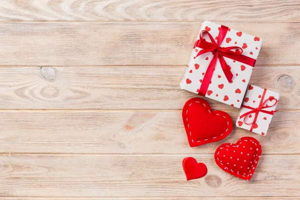 Sevgililer veya diğer tatil el yapımı mevcut kağıt ile tatil sarmalayıcı kırmızı kalpler ve hediye kutusunda. Tasarım için turuncu ahşap masa üstten görünüm kopya alanı ile boş alanı hediye kutusu.