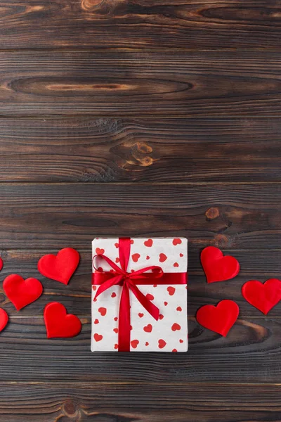 Sevgililer veya diğer tatil el yapımı mevcut kağıt ile tatil sarmalayıcı kırmızı kalpler ve hediye kutusunda. Tasarım için kopya alanı görünümüyle koyu ahşap masa üstü, boş alanı hediye kutusu.