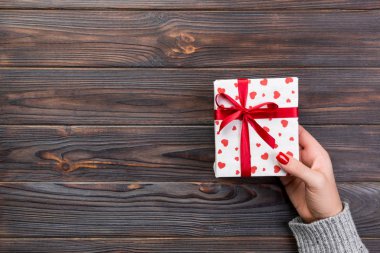 Kadın el kağıt kırmızı kurdele ile sarılmış Sevgililer veya diğer tatil el yapımı hediye vermek. Kopya alanı tasarım için hediye ahşap masa üzerinde üstten görünüm kutusunda, kırmızı kalp dekorasyon avantajlarıyla.