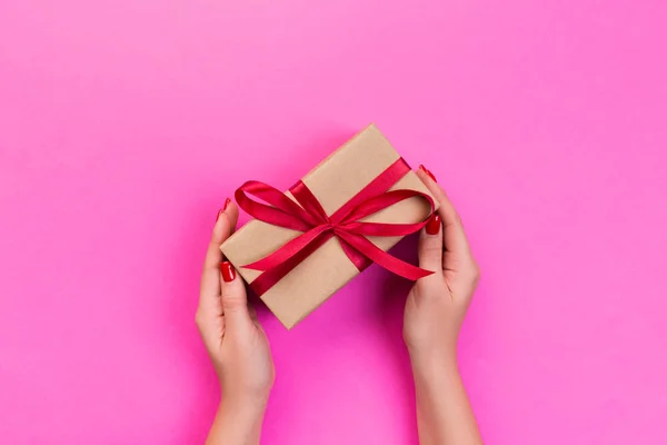 妇女的手给包装的情人节或其他节日手工礼物的纸与红色丝带 礼物盒 在粉红色桌子上的礼物装饰 顶部视图与复制空间 — 图库照片