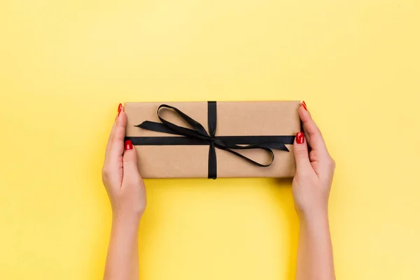 妇女的手给包装的情人节或其他节日手工礼物的纸与黑色丝带 礼品盒 黄色桌子上的礼品装饰 带复印空间的顶视图 — 图库照片