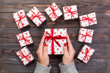 Kadın el kağıt kırmızı kurdele ile sarılmış Sevgililer veya diğer tatil el yapımı hediye vermek. Kopya alanı tasarım için hediye ahşap masa üzerinde üstten görünüm kutusunda, kırmızı kalp dekorasyon avantajlarıyla.