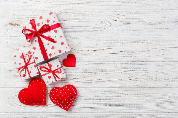 Valentine or other holiday handmade present in paper with red hearts and gifts box in holiday wrapper. Present box of gift on white wooden table top view with copy space, empty space for design.