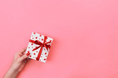 Kadın el kağıt kırmızı kurdele ile sarılmış Sevgililer veya diğer tatil el yapımı hediye vermek. Mercan rengi tablo hediye, üstten görünüm kutusunda, kırmızı kalp dekorasyon tasarım için kopya alanı ile mevcut.