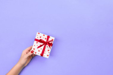 Kadın el kağıt kırmızı kurdele ile sarılmış Sevgililer veya diğer tatil el yapımı hediye vermek. Kopya alanı tasarım için hediye menekşe masada, üstten görünüm kutusunda, kırmızı kalp dekorasyon avantajlarıyla.