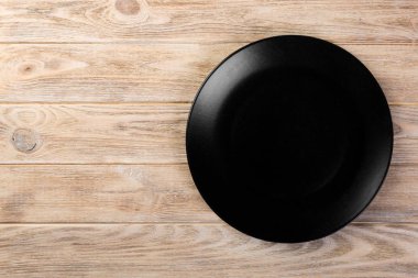 Directy turuncu ahşap arka plan kopya alanı ile akşam yemeği için boş siyah mat çanak yukarıda.