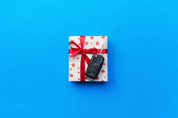 Give gift car key concept top view. Present box with red ribbon bow, heart and car key on blue colored background.