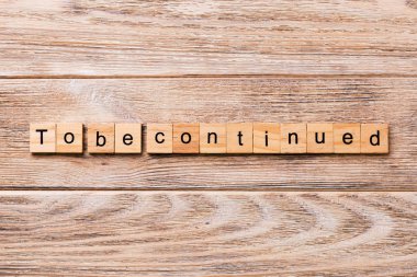 To be continued word written on wood block. To be continued text on wooden table for your desing, concept. clipart
