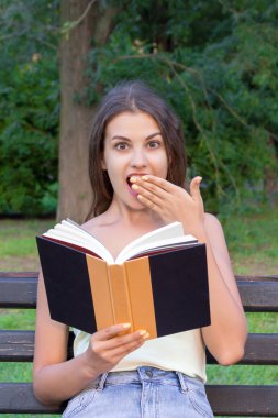 Sürpriz güzel kız bir kitap okuma ve elinle ağzını kapsayan
