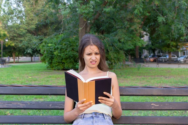 Mulher chocada e surpreso está segurando um livro e tem olhar descontente — Fotografia de Stock