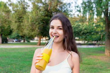 Çekici kız dışarıda pipetten taze meyve suyu içiyor. Güzel kadın elinde bir şişe soğuk limonata tutuyor.