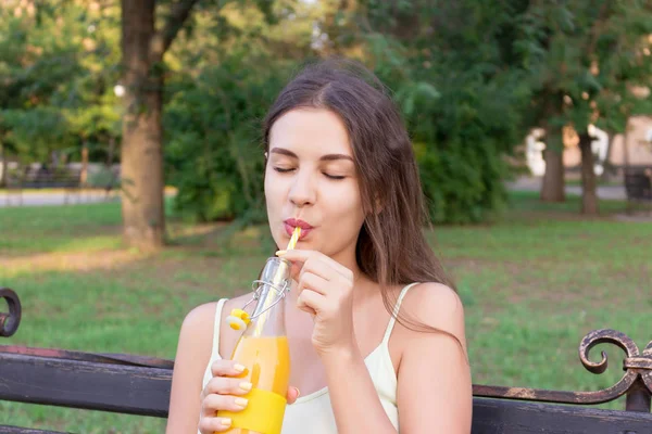 Ung vacker kvinna med en flaska färsk apelsinjuice njuter av ett bra väder i parken — Stockfoto