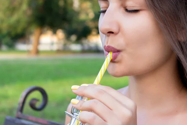 Ung vacker kvinna med en flaska färsk apelsinjuice njuter av ett bra väder i parken — Stockfoto