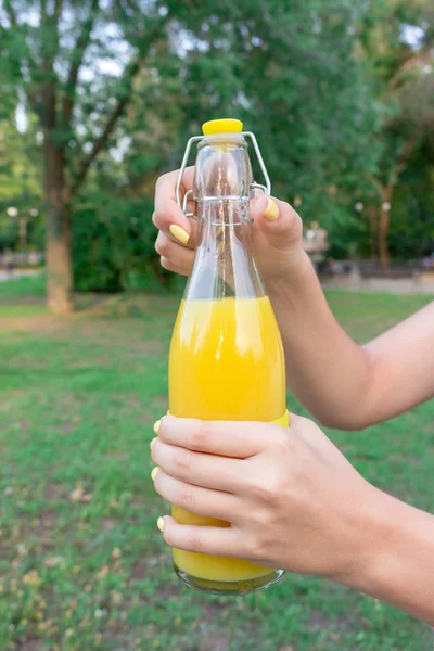 Imagen recortada de una chica que sostiene y abre una botella de jugo fresco afuera — Foto de Stock