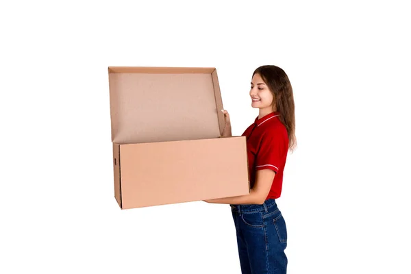 Smiling delivery woman is looking into open cardboard box, post delivery concept, isolated on white background — стоковое фото