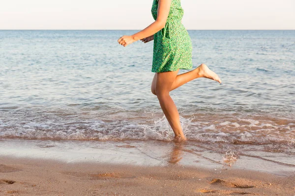 Ben av kvinnan som kör på stranden med vatten stänk. Sommarlovet. benen på en flicka som går i vatten på solnedgång — Stockfoto
