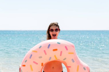 Güzel çılgın kadın rahatlatıcı ve deniz plajında şişme halka ile oynuyor. Yaz tatilleri ve tatil konsepti