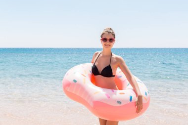Yüzme havuzunda güzel genç kadın şişme halka donut yüzer ve tatilde kokteyl cam ile eğleniyor