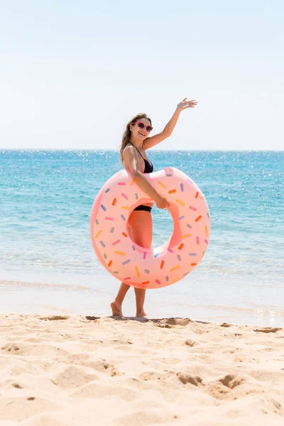Mujer llama a nadar en el mar y agita su mano. Chica relajándose en el anillo inflable en la playa. Vacaciones de verano y concepto de vacaciones —  Fotos de Stock