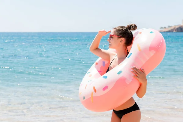 Наслаждаюсь солнцем и отдыхом. Портрет счастливой девушки, смотрящей через надувное кольцо, останавливается на морском пляже. Концепция летнего отдыха — стоковое фото
