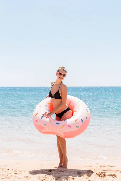Mulher bonita na piscina nada no donut inflável do anel e se diverte com um copo de coquetel de férias — Fotografia de Stock