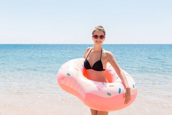 Красивая молодая женщина в бассейне плавает на надувном кольце пончика и весело проводит время со стаканом коктейля в отпуске — стоковое фото