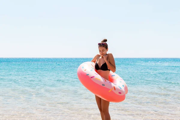 Молодая женщина с надувным кольцом холодная дрожащая грустные скрещенные руки черного бикини купальник, стоящий в морской воде. Летние каникулы и отдых — стоковое фото
