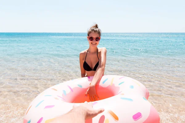 Follow me Vacation concept. girlcalls to swim in the sea and waves her hand. Girl relaxing on inflatable ring in the sea. Summer holidays