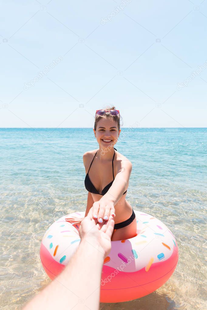 Follow me Vacation concept. girlcalls to swim in the sea and waves her hand. Girl relaxing on inflatable ring in the sea. Summer holidays