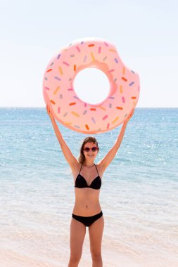 şişme bir donut halkası ile oynarken sahilde mutlu kadın. Yaz tatilleri ve tatil konsepti
