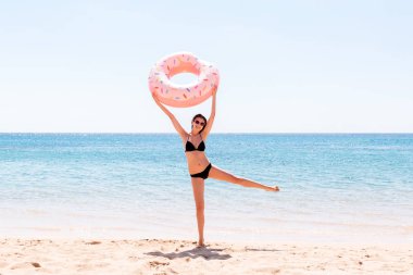 Sahilde şişme çörek halkasıyla oynayan mutlu bir kadın. Yaz tatilleri ve tatil konsepti
