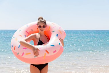 Yaz güneşli bir günde plajda şişme donutla yüzen bir kadın. Yaz tatili ve tatil konsepti